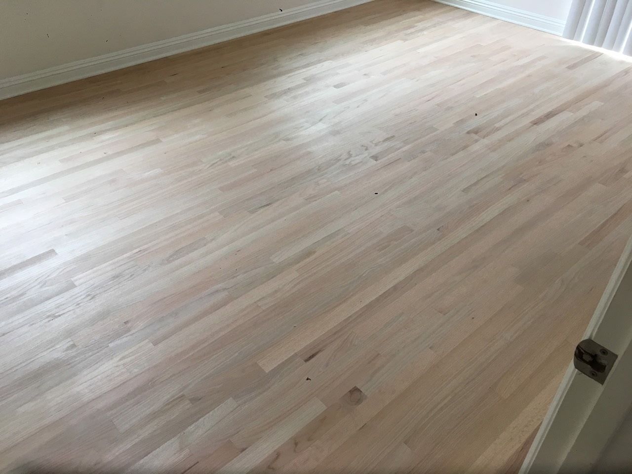 A recently sanded light-colored hardwood floor in a room, viewed from an entryway.