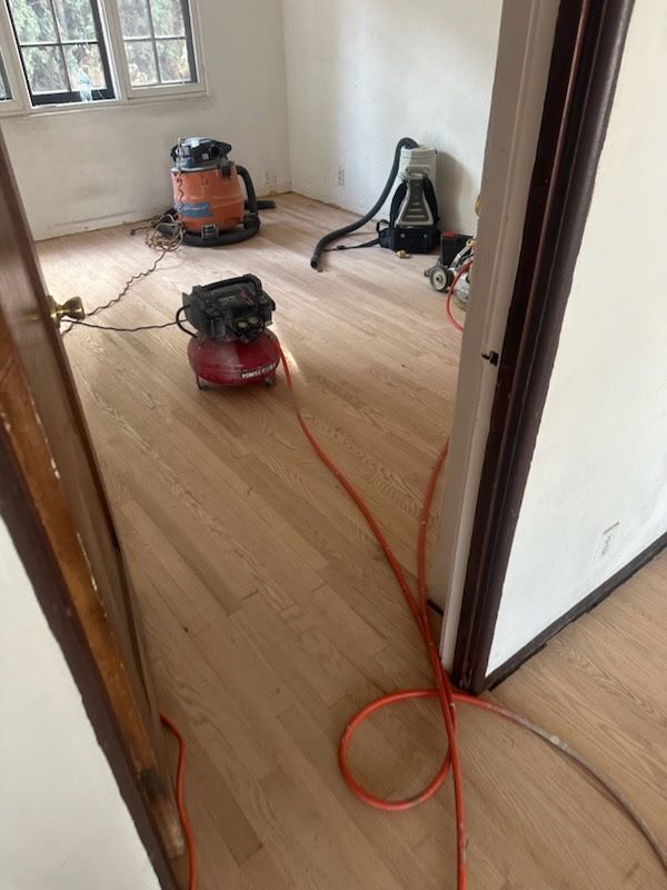 A room with newly sanded hardwood floors, featuring several pieces of industrial construction equipment and power cables.