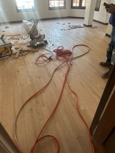 Construction site with light hardwood flooring, tools, and a coiled orange extension cord in an unfinished room.