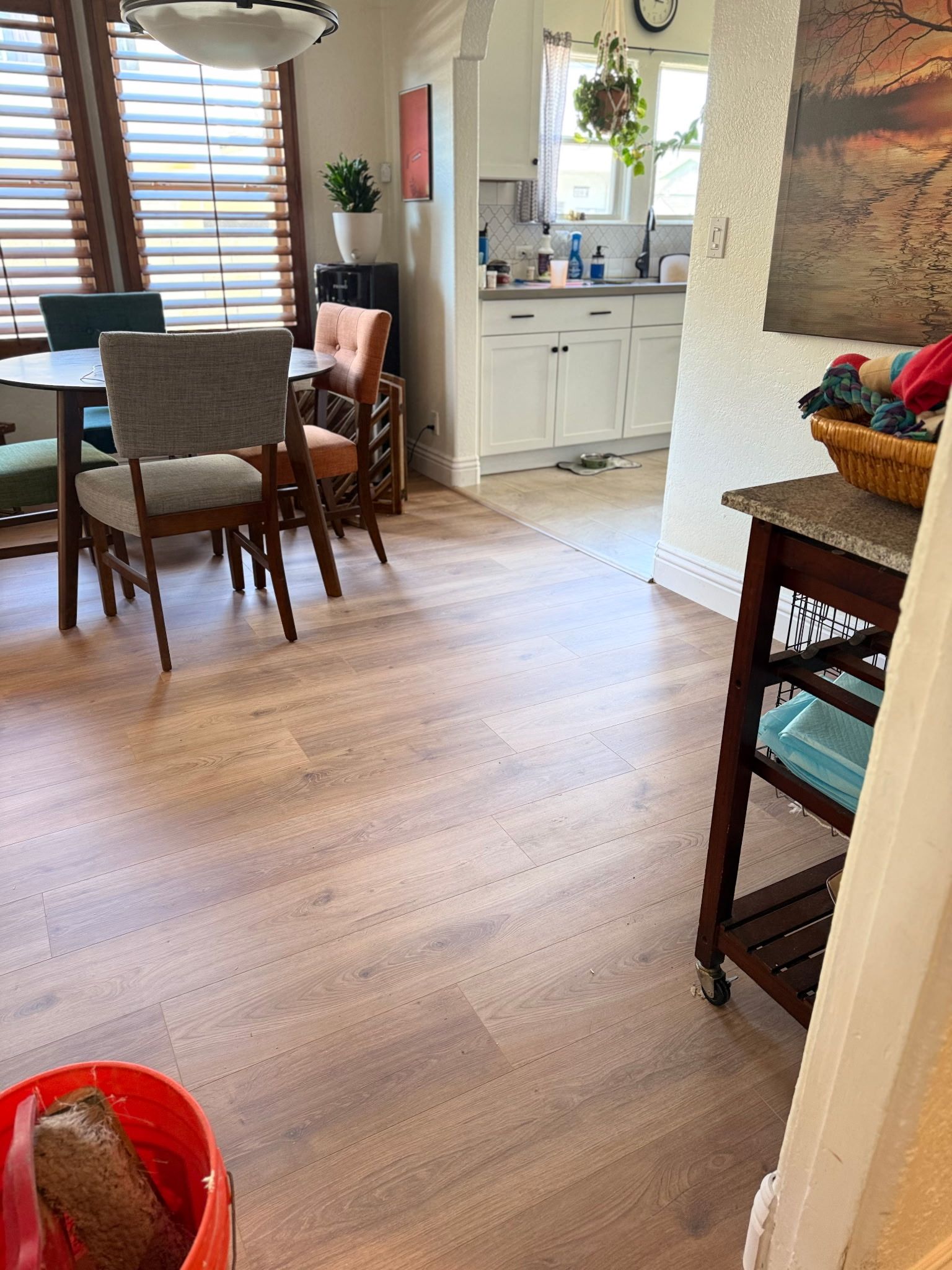 A room with light wood flooring, a dining table and chairs, and a doorway leading to a white kitchen.