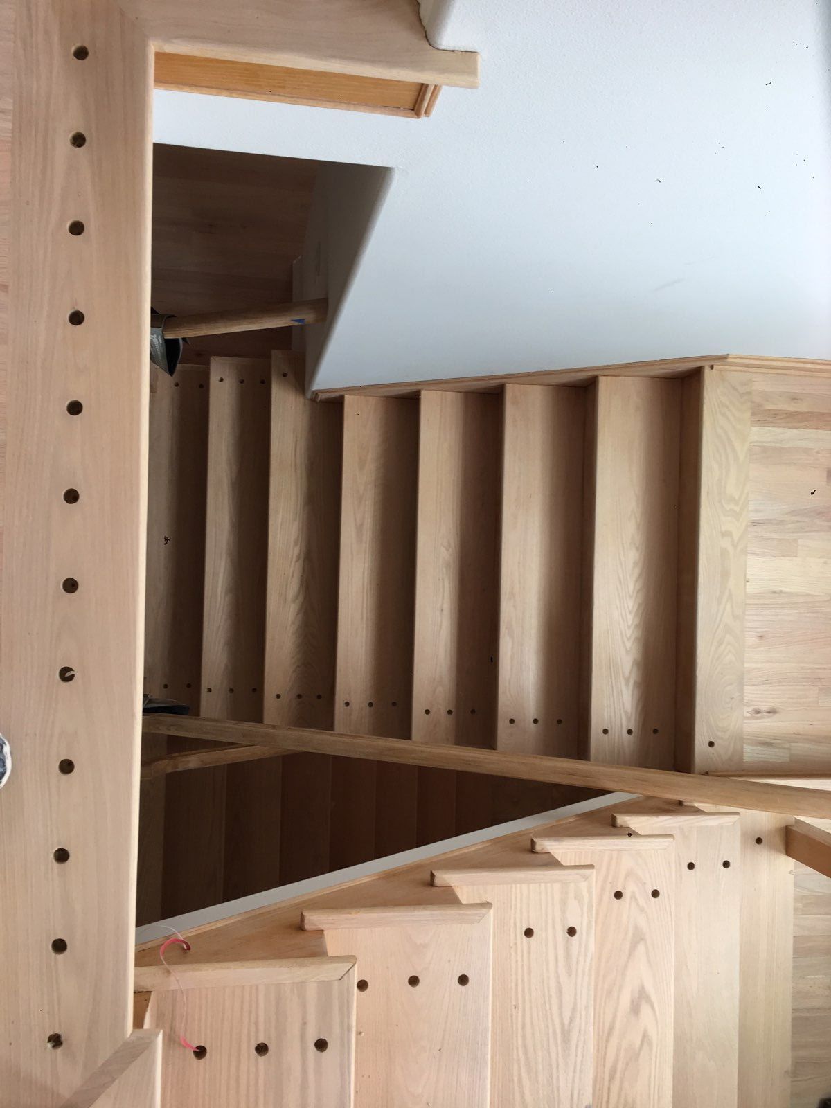A top-down view of unfinished wooden stairs leading to a lower level, featuring dark circular nail holes along the edges.