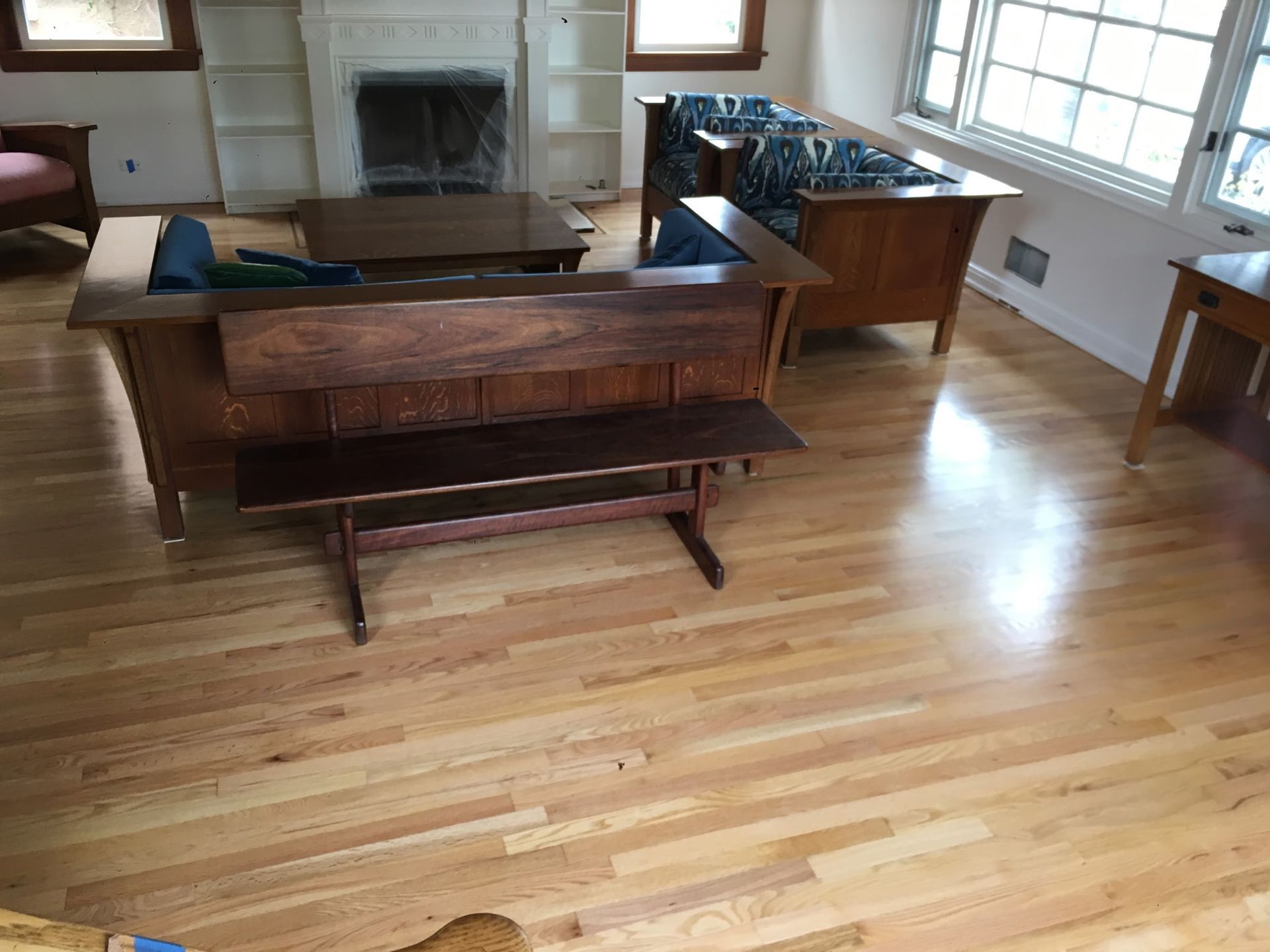A brightly lit living room featuring light hardwood floors, wooden mission-style furniture, and a stone fireplace.