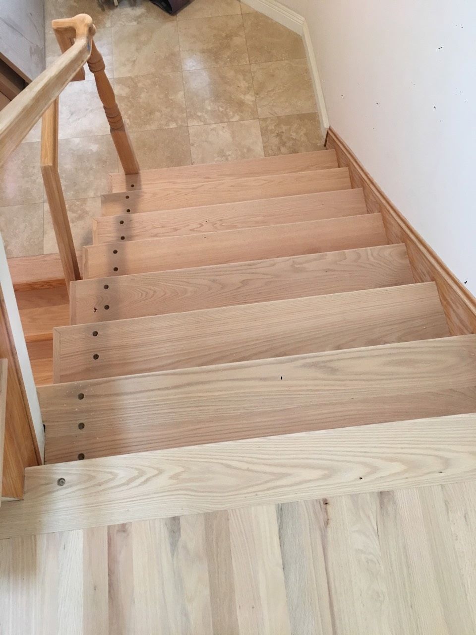 Looking down a set of light-colored wooden stairs with a handrail on the left, leading to a tiled landing.