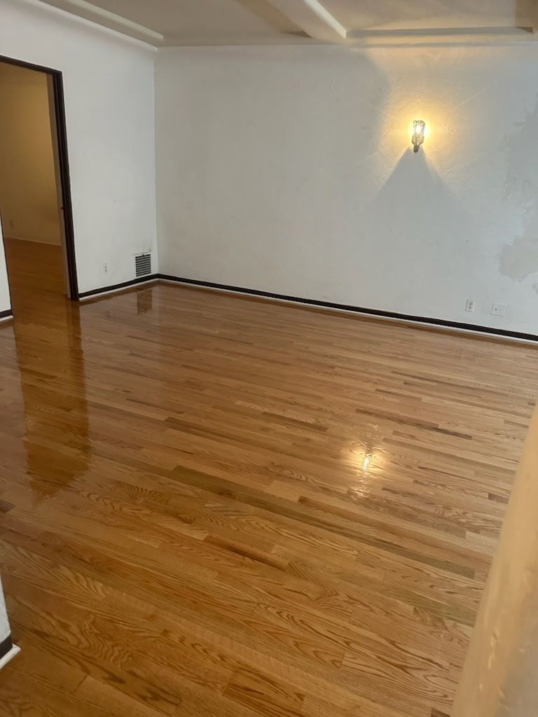 An empty room with light-colored hardwood floors, white walls, a dark trim along the floor, and a wall sconce.