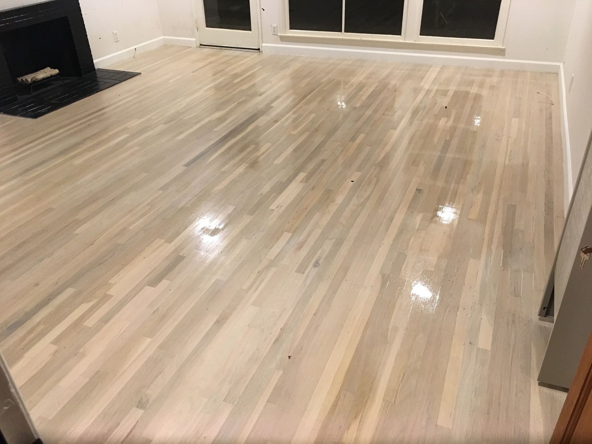A room featuring freshly refinished light-toned hardwood flooring with a glossy sheen and a black fireplace.