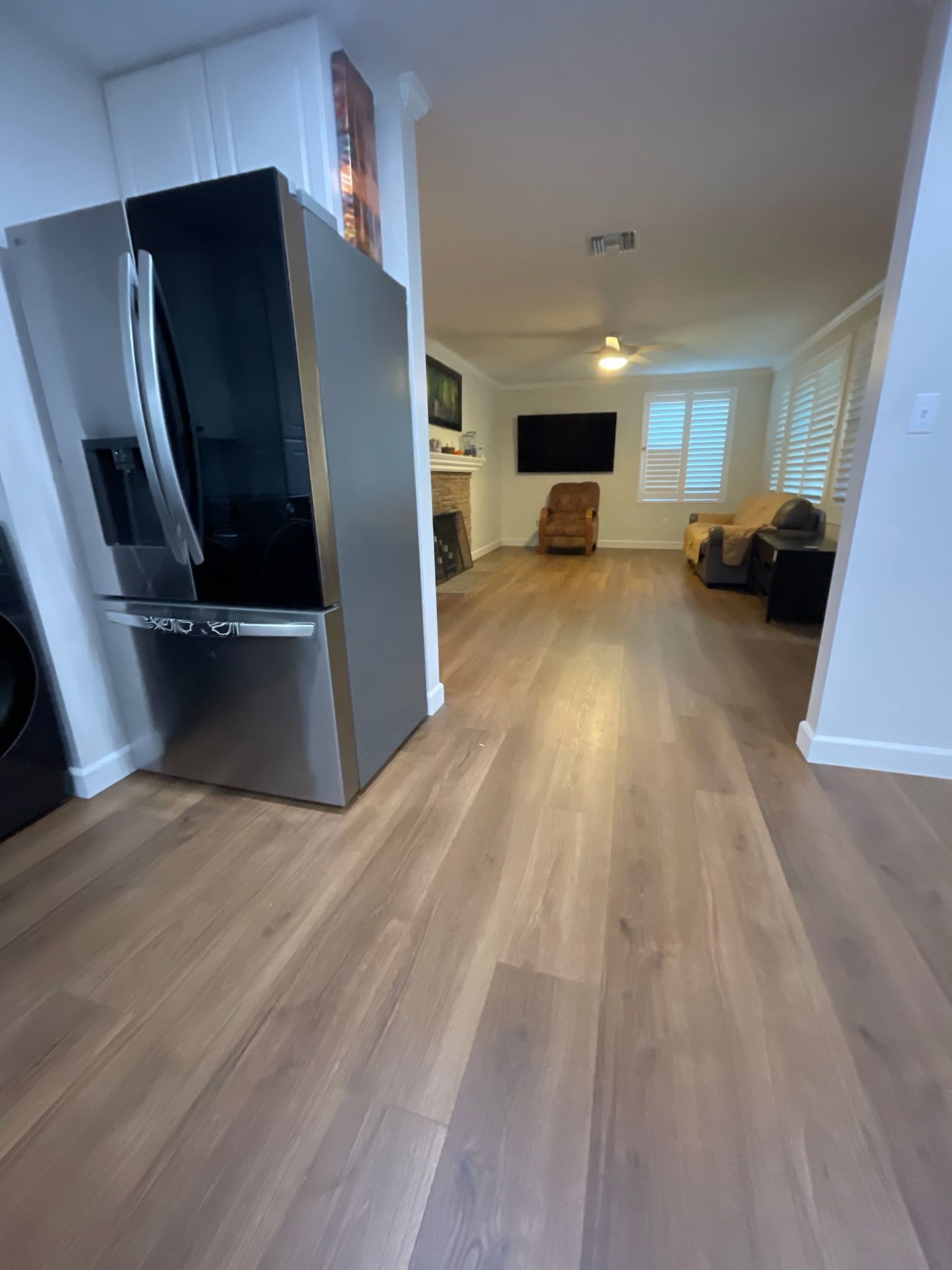 Modern kitchen refrigerator in the foreground, with an open-plan living room featuring wood floors and a seating area.