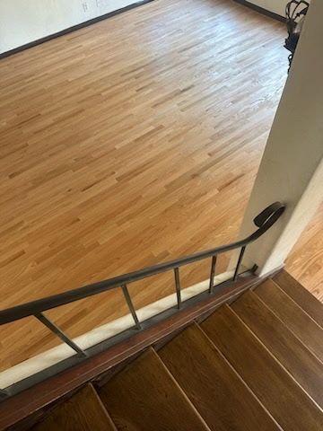 A high-angle view looking down a wooden staircase with a dark metal railing toward a light-toned hardwood floor.