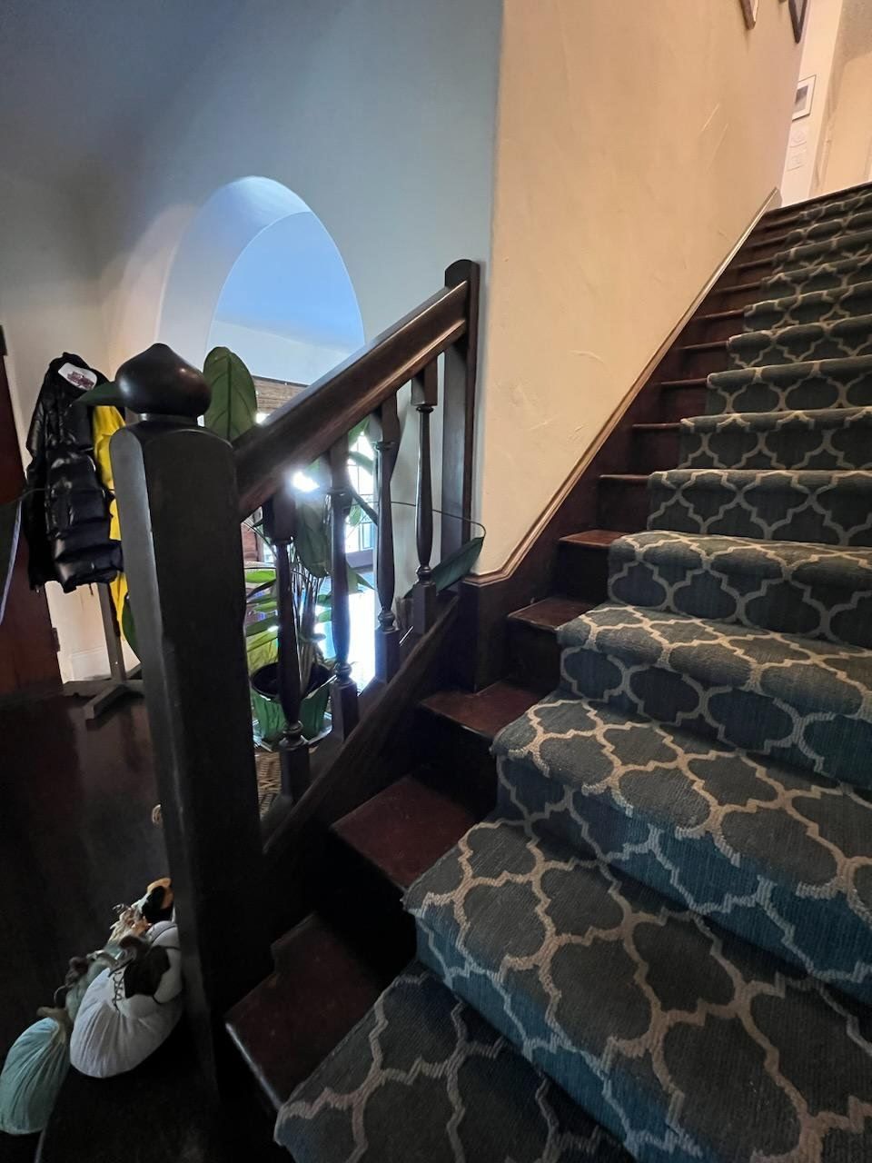 A staircase with dark wood railings and a teal carpet runner featuring a white geometric pattern, viewed from below.