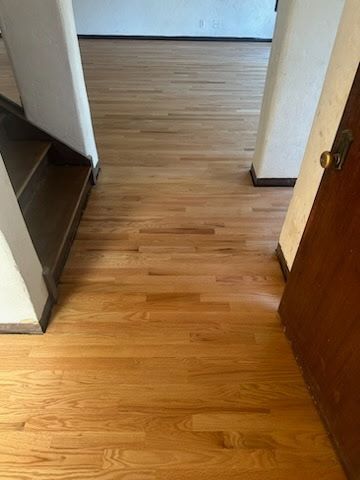 A light-colored hardwood floor transitions through an open doorway, with a wooden staircase visible to the left.