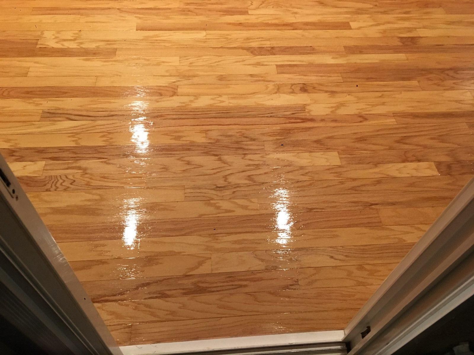 A view from a doorway looking down at a polished, light-brown hardwood floor with visible wood grain patterns.