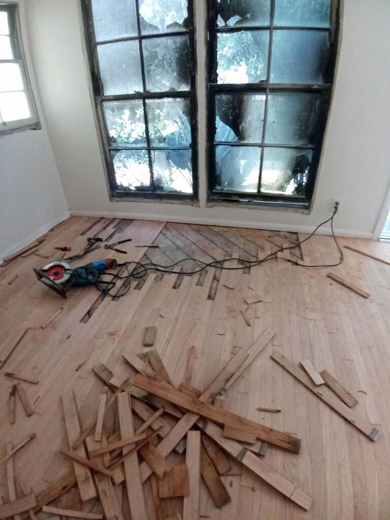 A room under renovation with hardwood flooring being installed, featuring a circular saw and wood scraps on the floor.