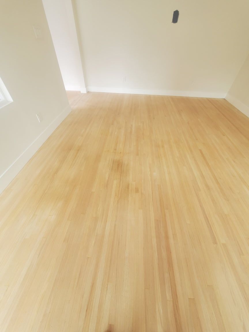A view looking across light-colored, unfinished hardwood flooring in an empty room with white walls.