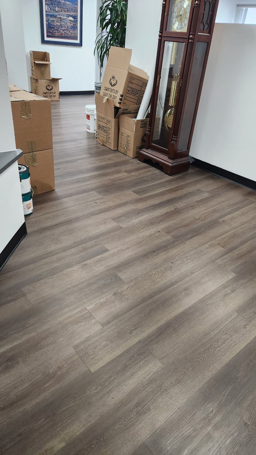 An office hallway with cardboard moving boxes stacked on the floor near a wooden grandfather clock.