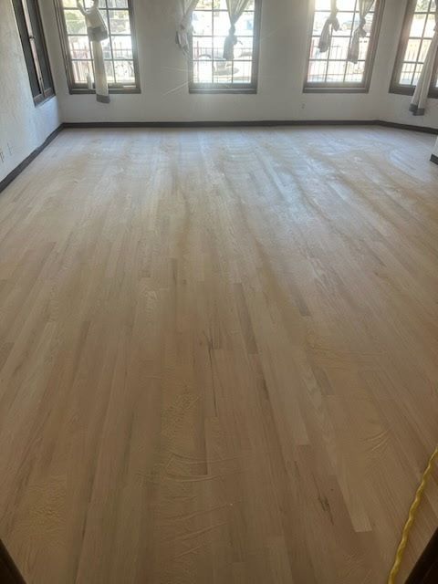 Newly sanded light-toned hardwood floor in a room with three large windows.
