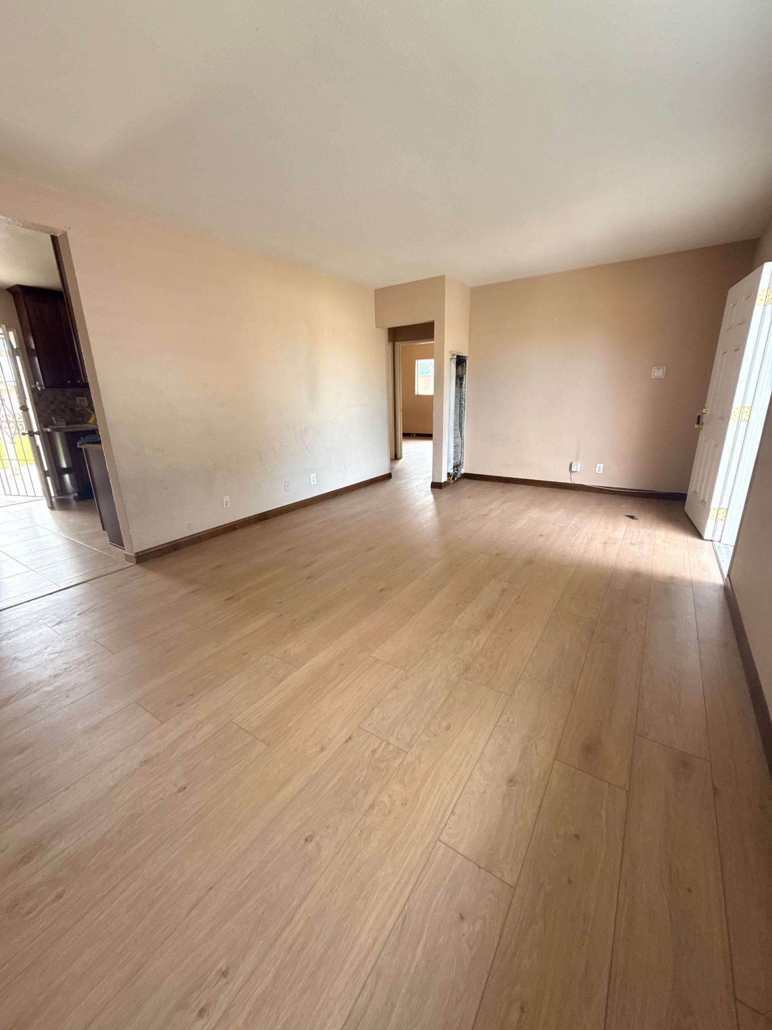 Empty room with light wood-tone laminate flooring, light beige walls, and doorways leading to other parts of the home.