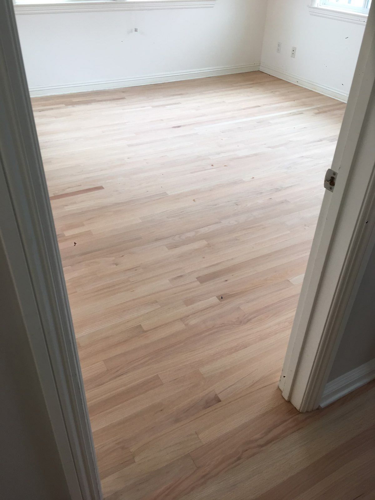 A view through a doorway into an empty room featuring recently sanded, unfinished light-colored hardwood floors.