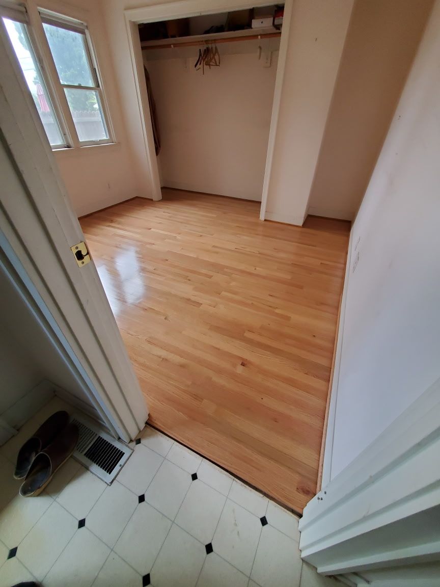 A view from a tiled entryway into a bedroom featuring polished hardwood floors, a closet, and a window with natural light.