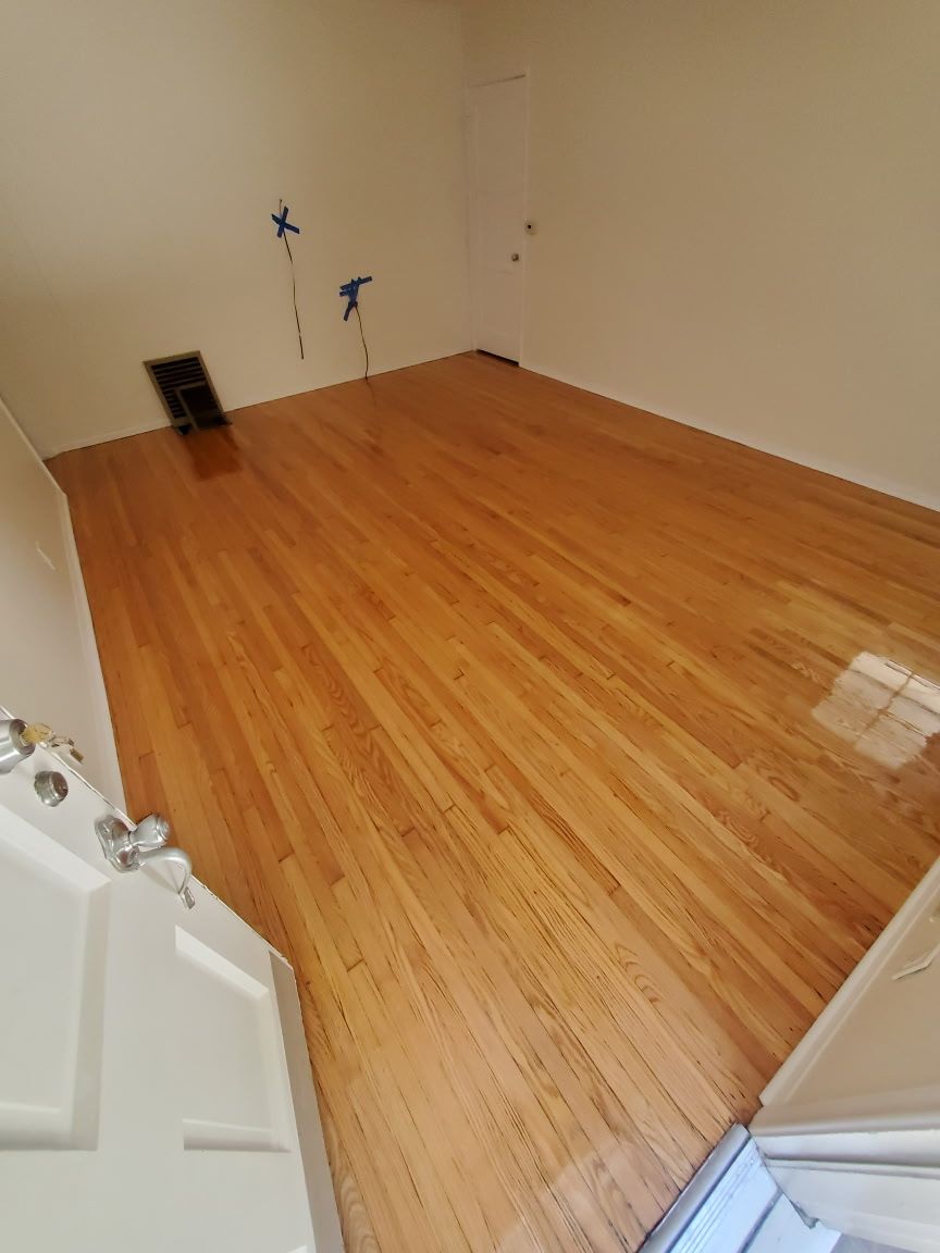 A view from a doorway into an empty room with polished light-wood floors and beige walls.