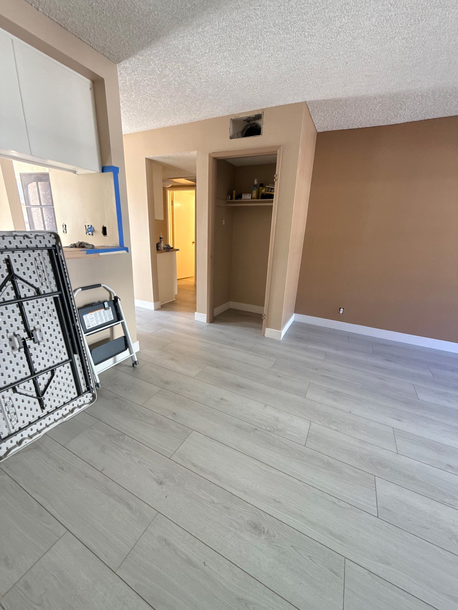 A room with light wood-look flooring, a beige wall, a small open closet, and a folded metal bed frame in the foreground.