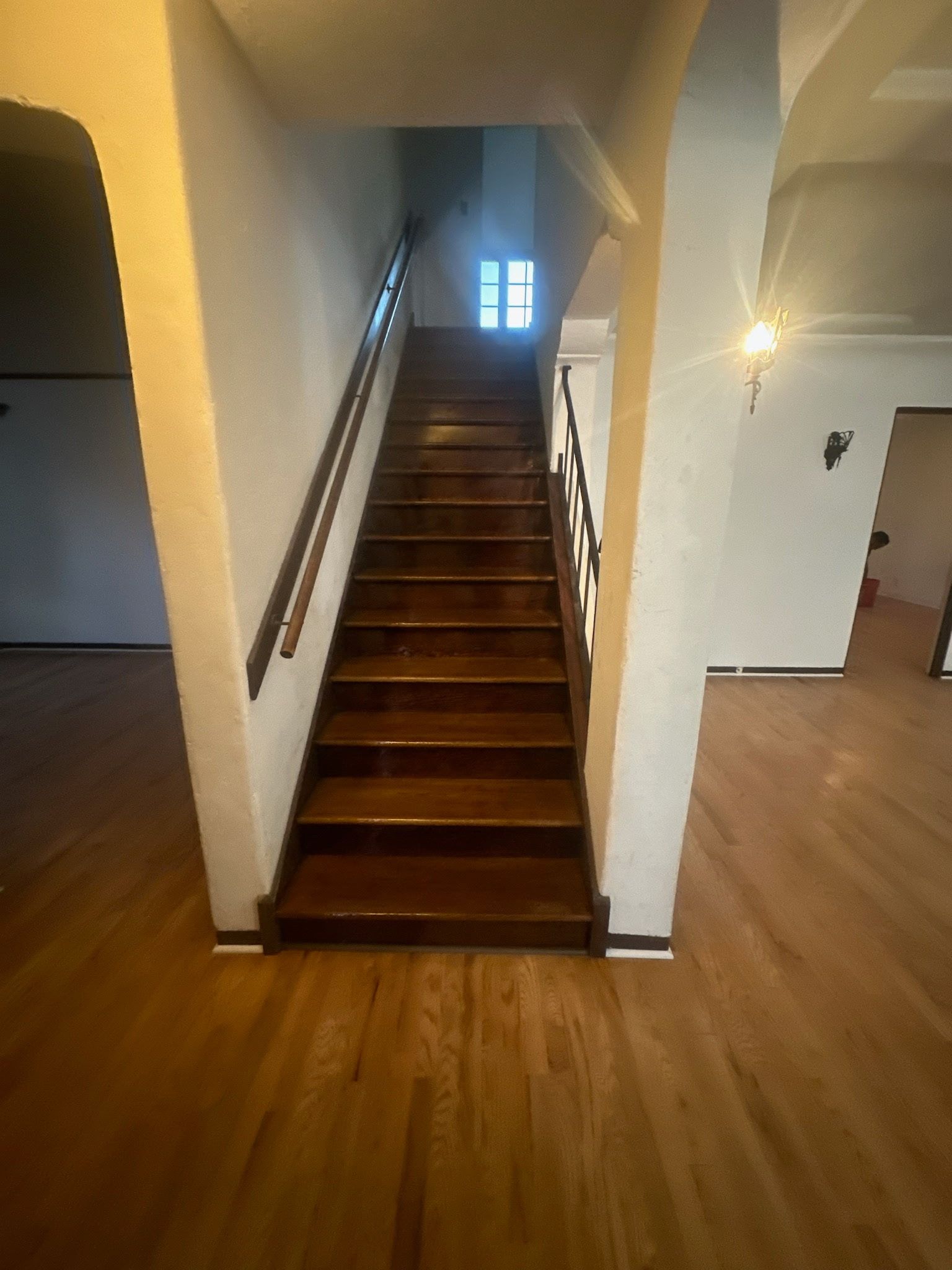 A straight wooden staircase leading upward between two white walls, viewed from a light-colored wood floor.