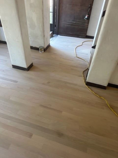 Light-toned wood flooring installed in a hallway with white columns and a dark wooden door in the background.