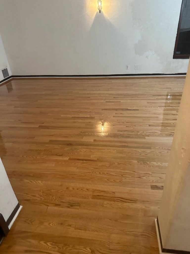 An empty room with polished light-colored hardwood floors and plain white walls under a single wall-mounted light.