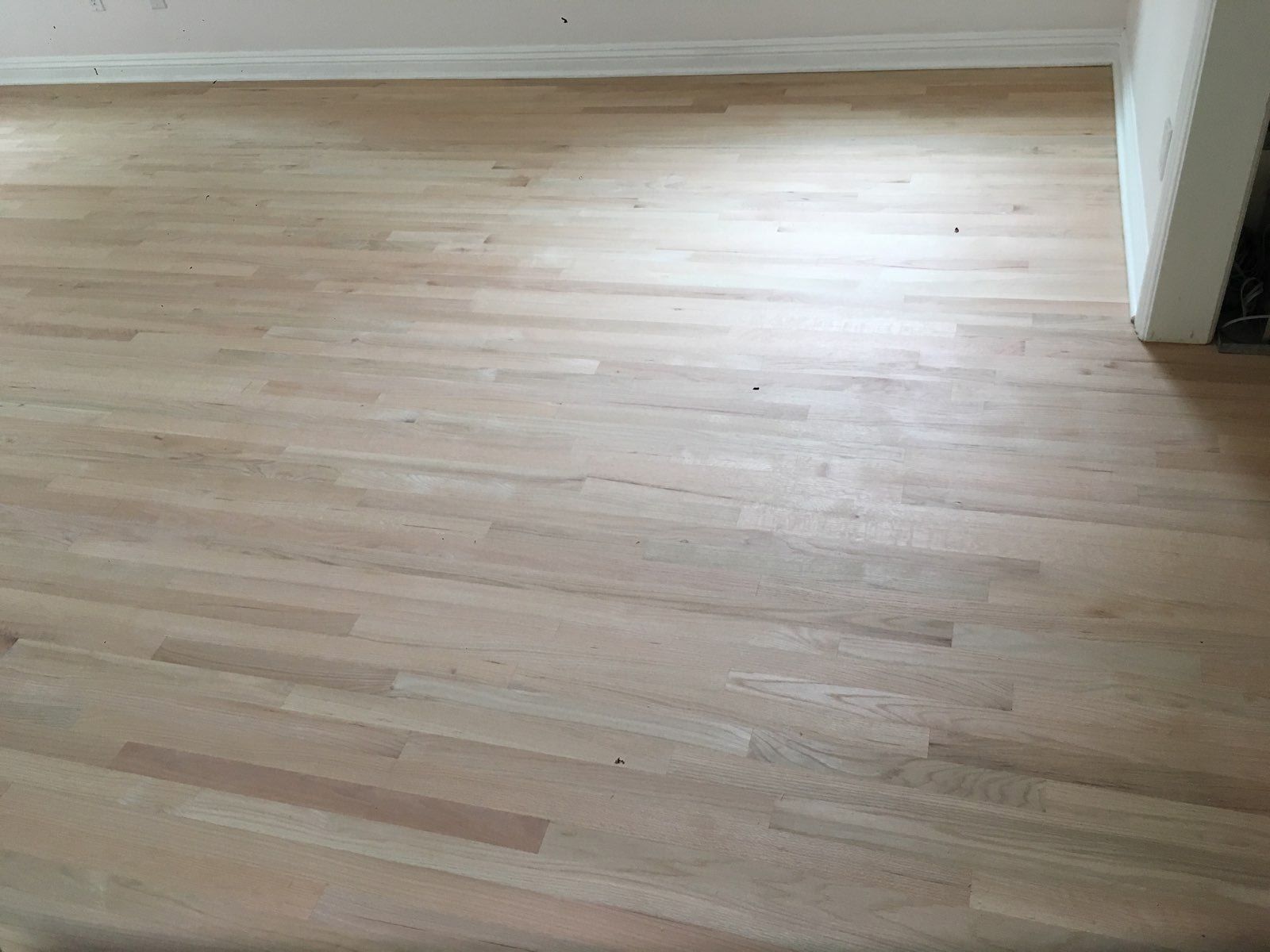 Unfinished light-colored hardwood floor boards with visible grain patterns inside a room.