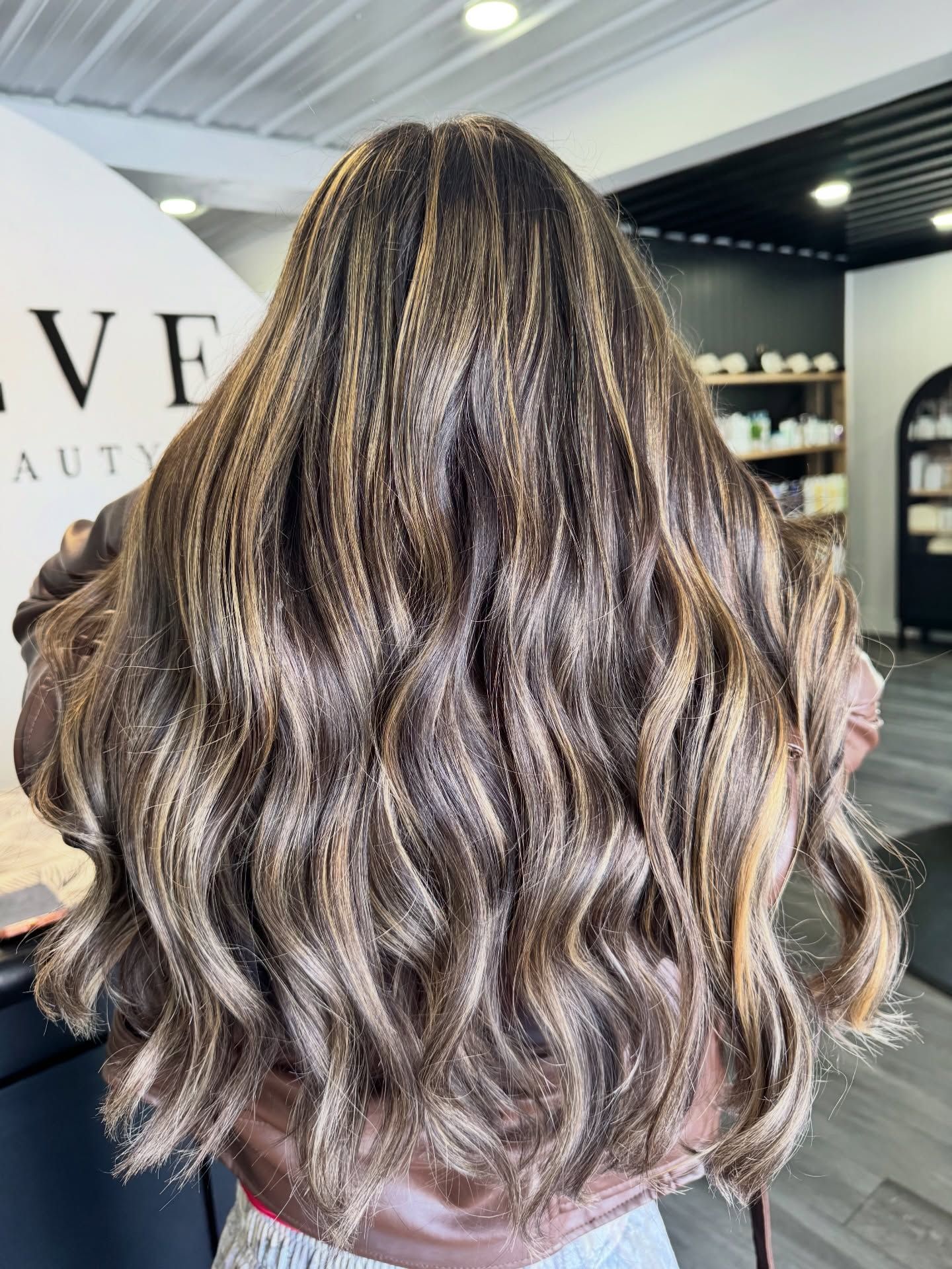Long wavy brown hair with blonde highlights; inside a beauty salon.