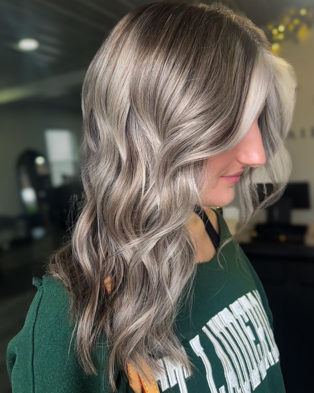 Woman with wavy ash brown and blonde hair, wearing a green sweater.