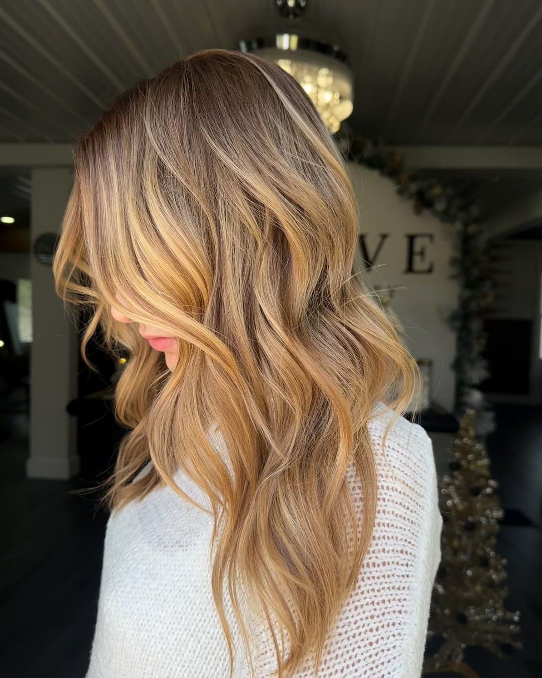 Woman with long, wavy, layered hair; brown to blonde balayage, soft lighting.