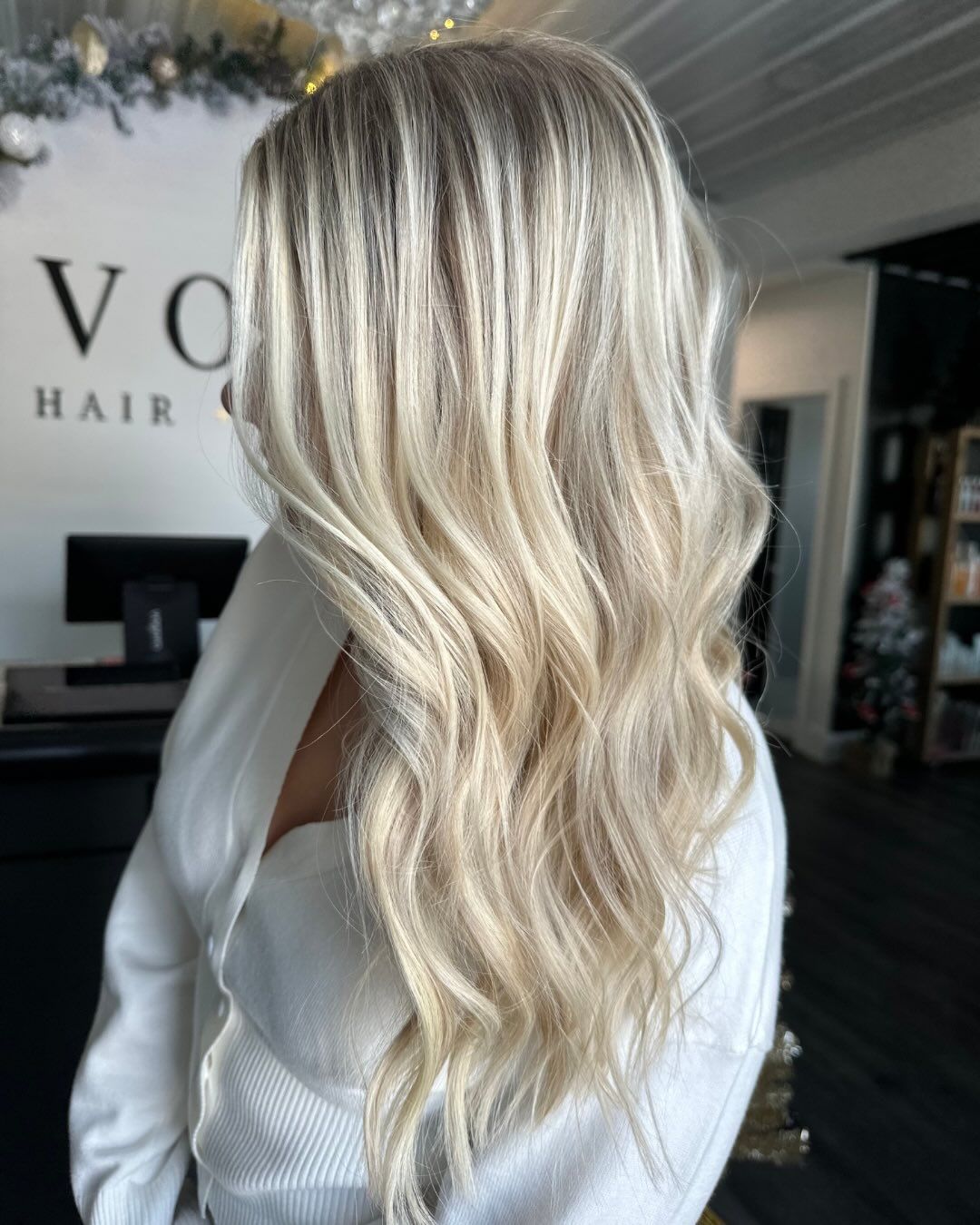 Woman with long, wavy, blonde hair, styled. She wears a white sweater.