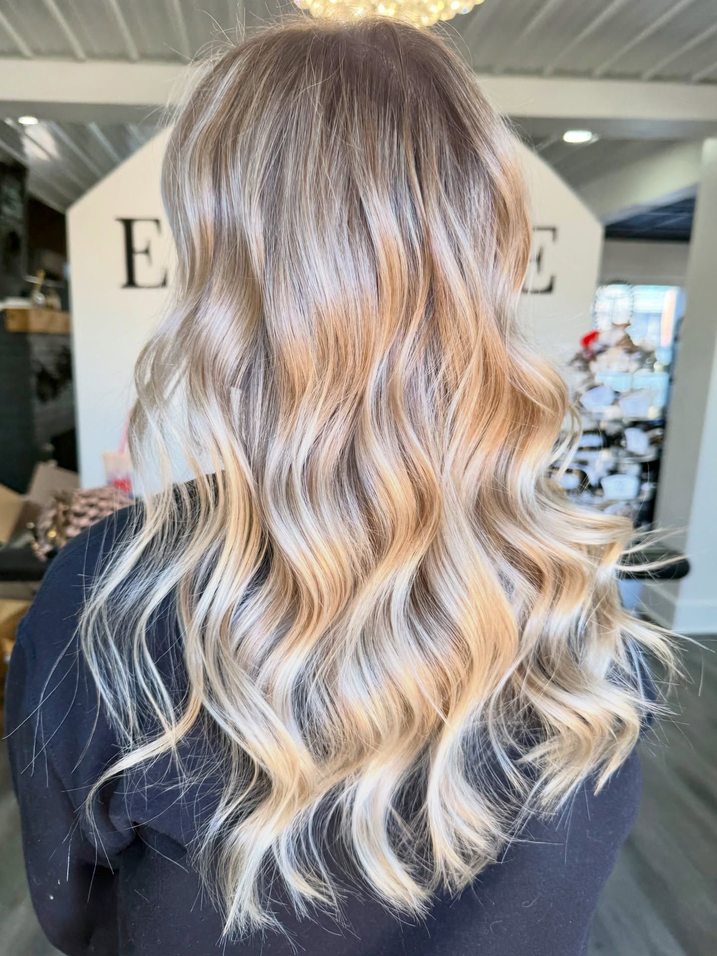 Woman with wavy, blonde and brown highlighted hair, styled in a salon.