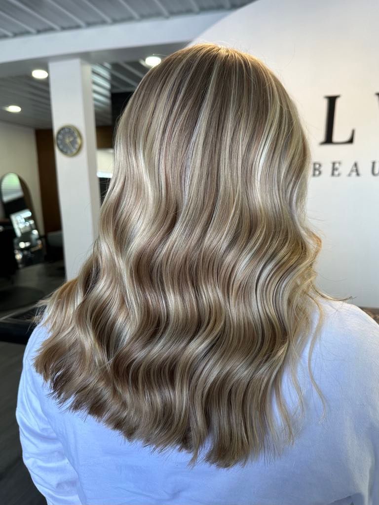 Woman with wavy, light brown hair with blonde highlights, styled in a salon.