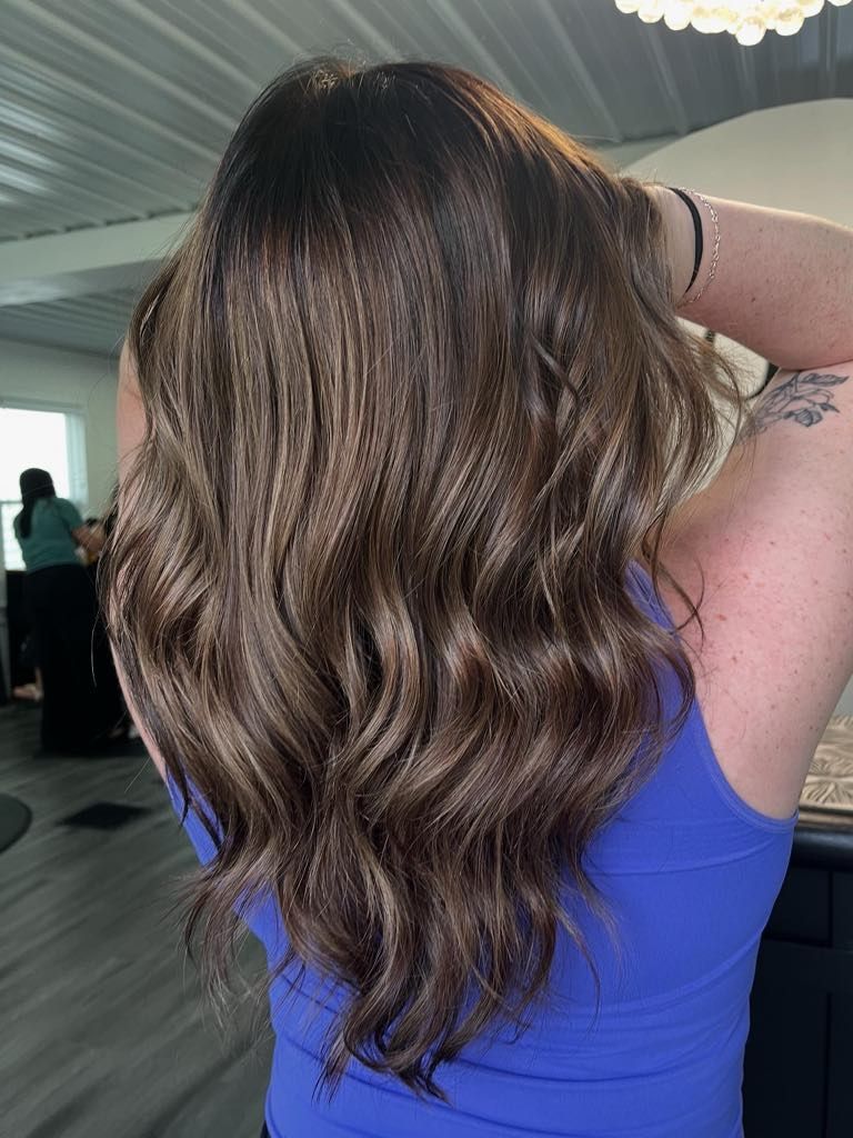 Woman with wavy, brown hair; wearing a blue tank top, inside a salon.