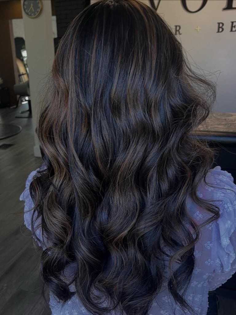 Woman with dark, wavy hair styled with subtle highlights at a salon.