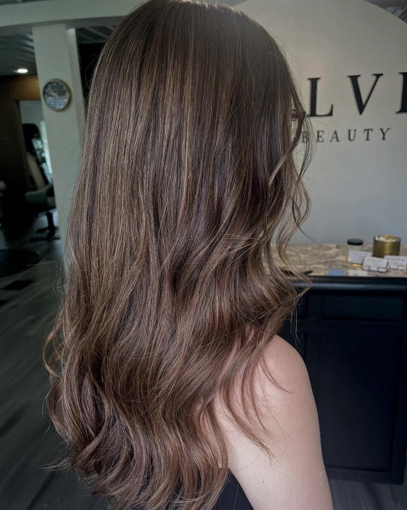 Woman with long, wavy, brown hair; salon interior.