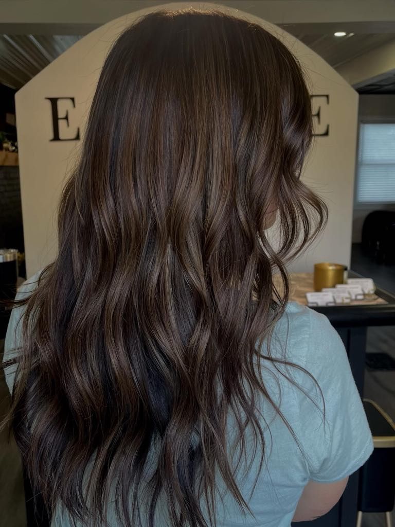 Woman with long, wavy, dark brown hair, in a salon.