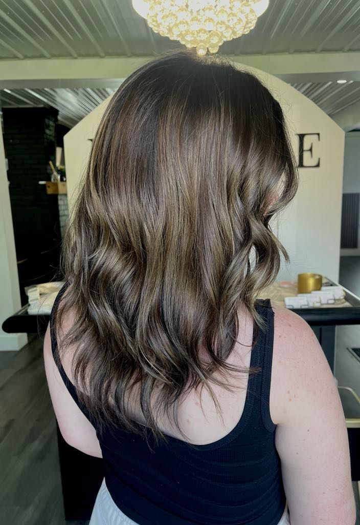 Woman with dark brown, wavy hair, wearing a black tank top, in a salon.
