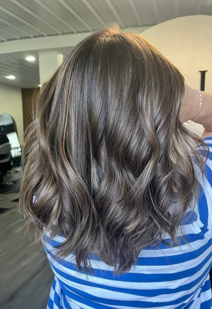 Woman with dark, wavy hair and blue and white striped shirt. Inside a salon.