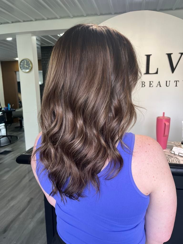 Woman with wavy brown hair, wearing a blue tank top, in a beauty salon.
