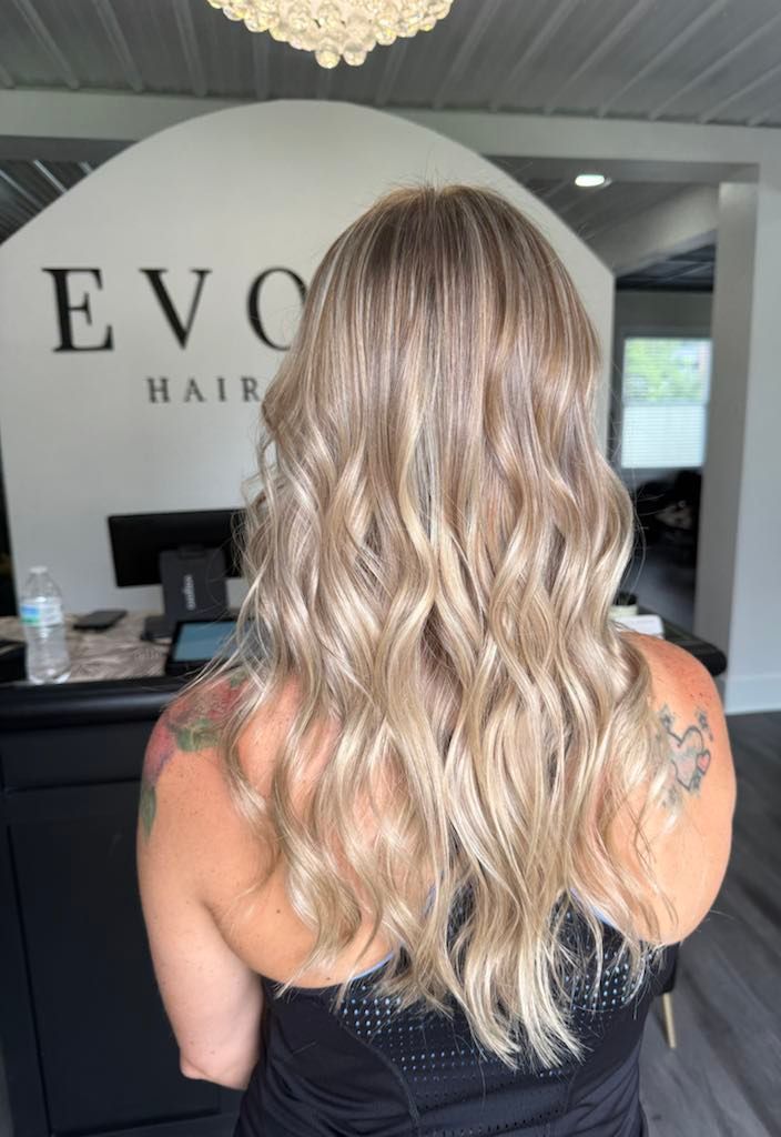 Woman with wavy blonde hair, arms turned away from camera, standing in a hair salon. 