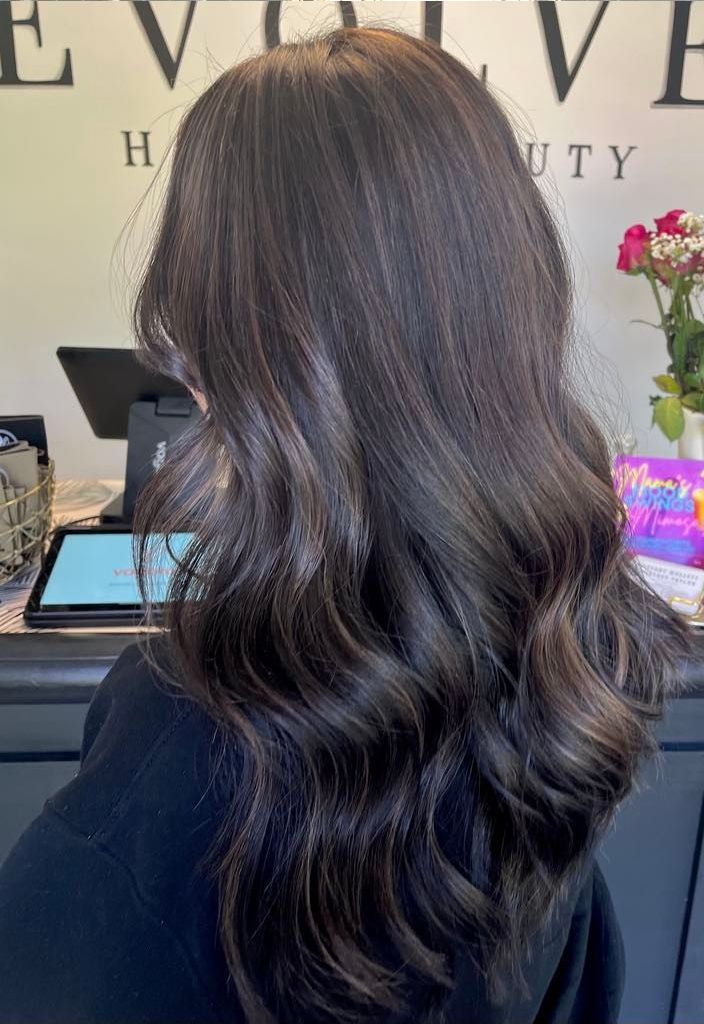 Woman with dark brown wavy hair with subtle highlights in a salon setting.