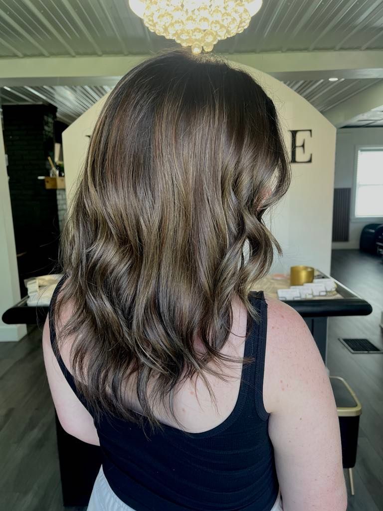 Woman with dark brown wavy hair with highlights in a salon setting.