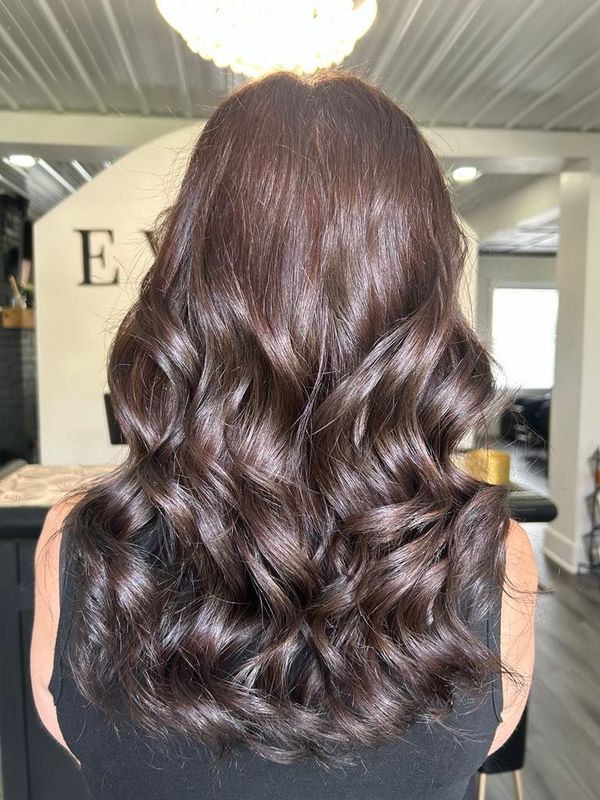 Woman with dark wavy hair styled in loose curls at a salon.