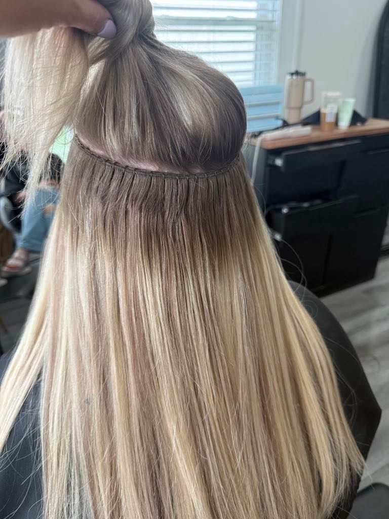 Close-up view of hair extensions being installed; the natural hair is dark at the roots, blending into lighter, layered extensions.