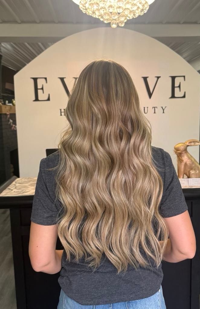 Woman with long, wavy, light brown hair, stands with back to the camera in front of a beauty salon sign.