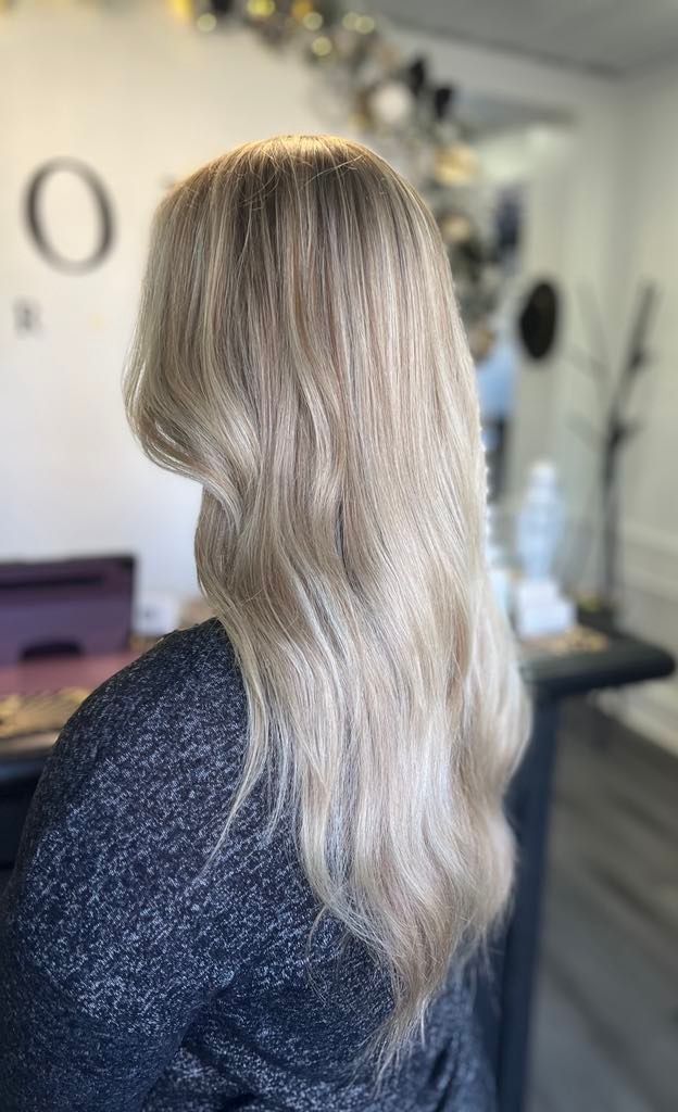 Woman with long, textured blonde hair; standing indoors.