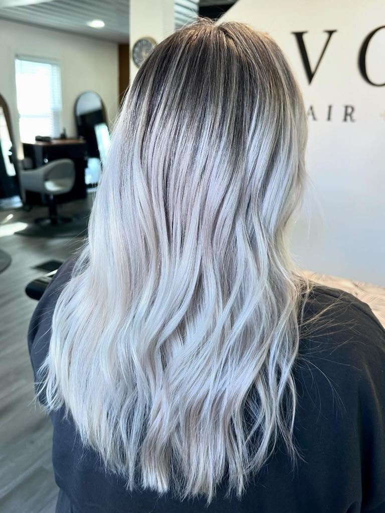 Woman with long, crimped, silver-blonde hair, dark roots, in a salon setting.