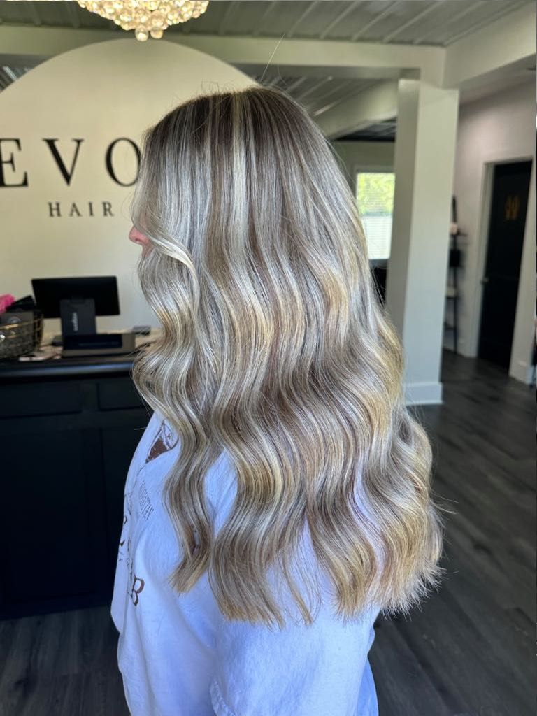 Woman with wavy, highlighted blonde hair in a salon setting.