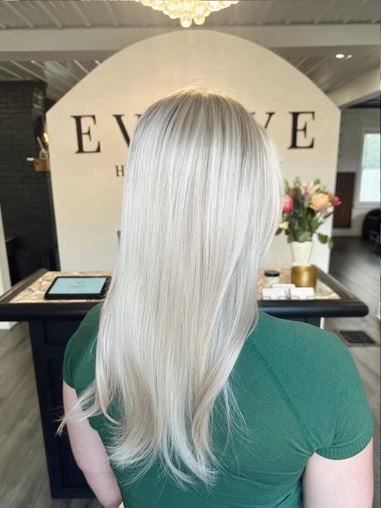 Woman with long, light blonde hair in a salon; green top. Background: 